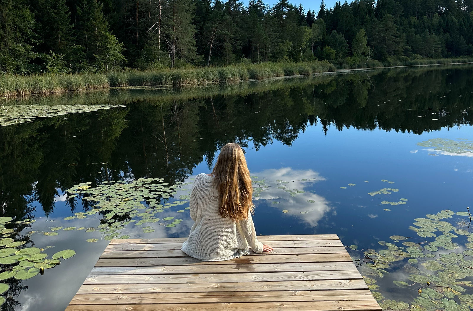 Girl sitting at a body of water, reflecting.