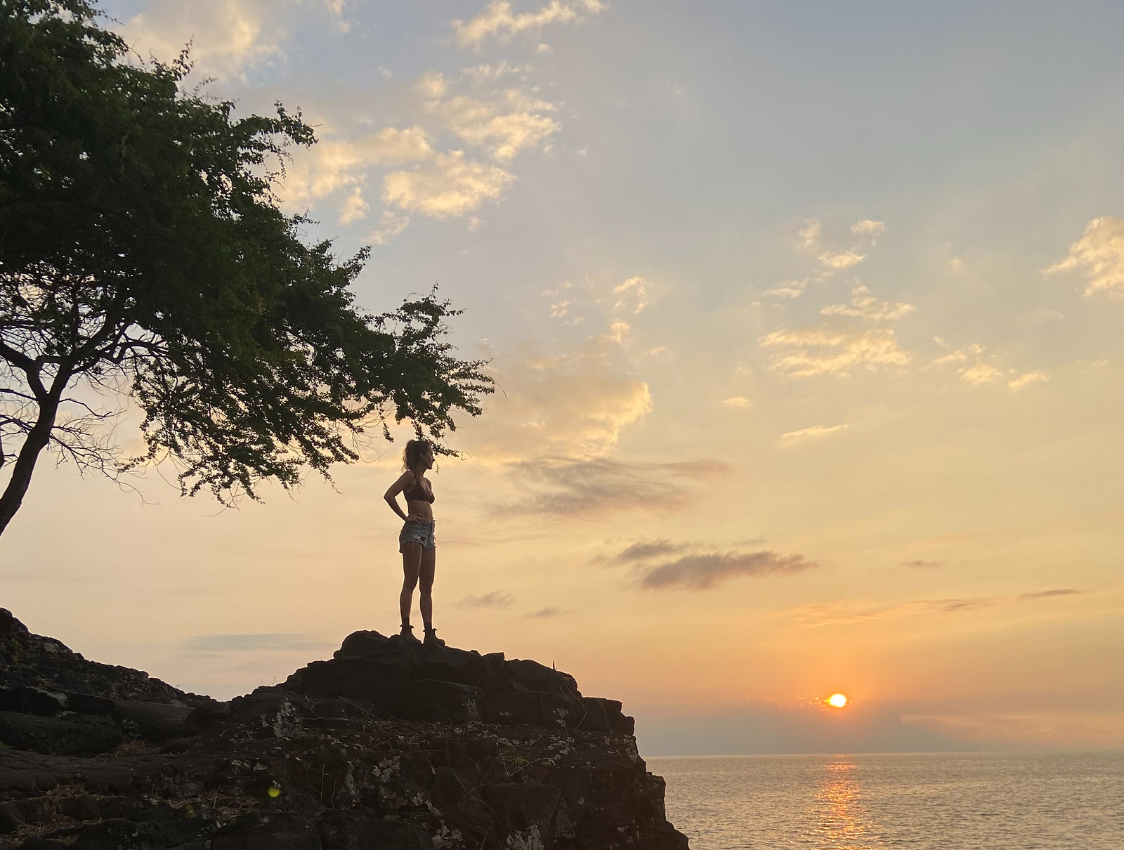 A woman standing on a rock watching the sunset
